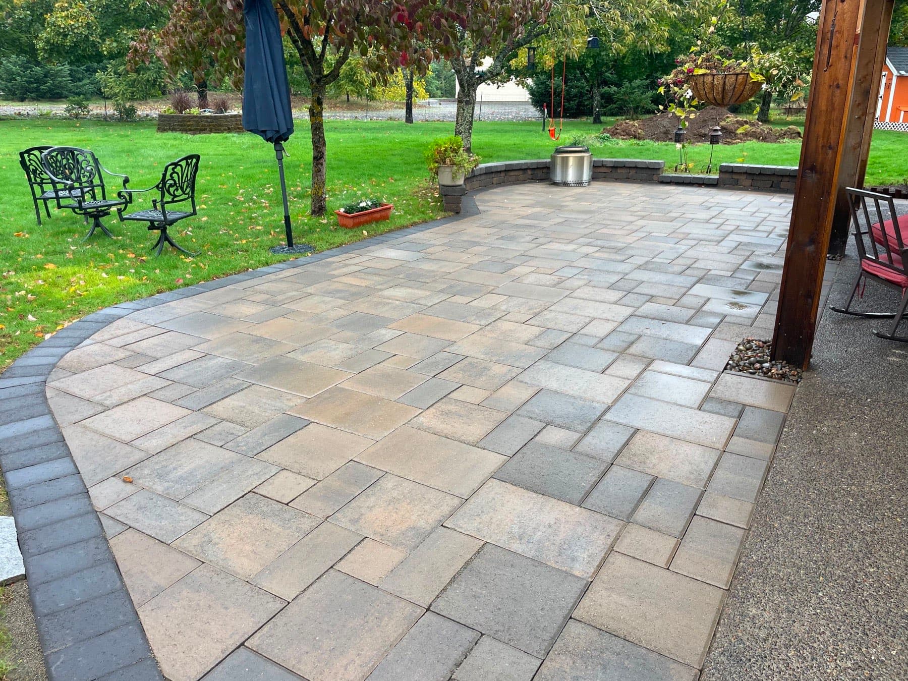 Large tan paver patio with a curved seat wall, fire pit and pergola post, laid in a random pattern by GI Landscape