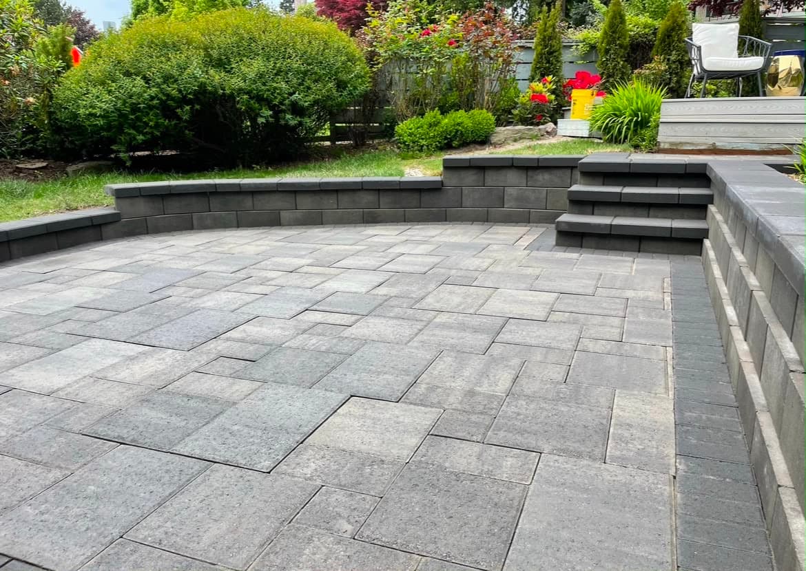 Grey paver patio enclosed by a curved charcoal seat wall with matching steps, installed by GI Landscape