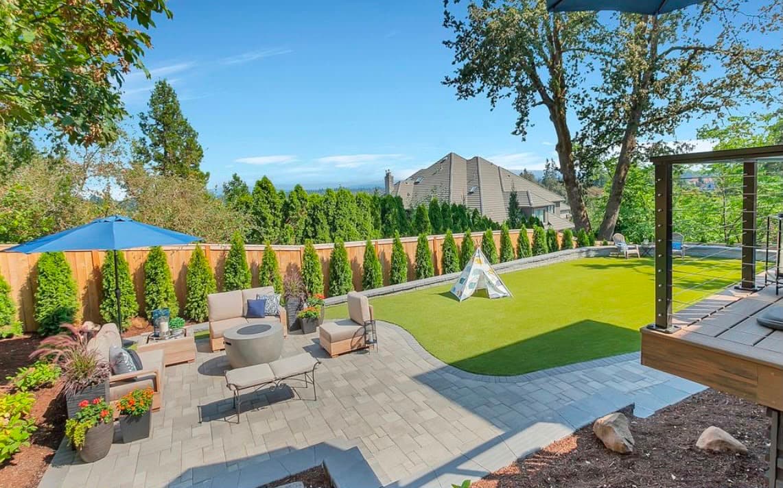 Wide backyard with paver patio lounge seating, fire table, artificial turf lawn and a cable-rail deck overlooking the valley, by GI Landscape