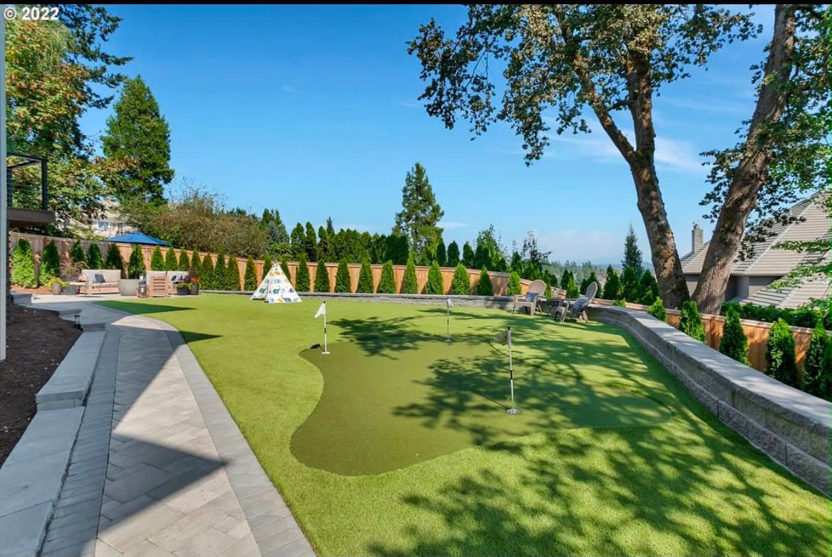Backyard artificial turf lawn with a built-in putting green, paver patio and block retaining wall, by GI Landscape