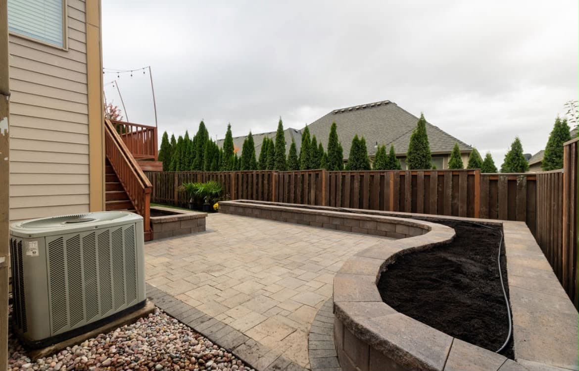 Paver patio with tiered block retaining walls and a curved raised planter bed on drip irrigation, by GI Landscape