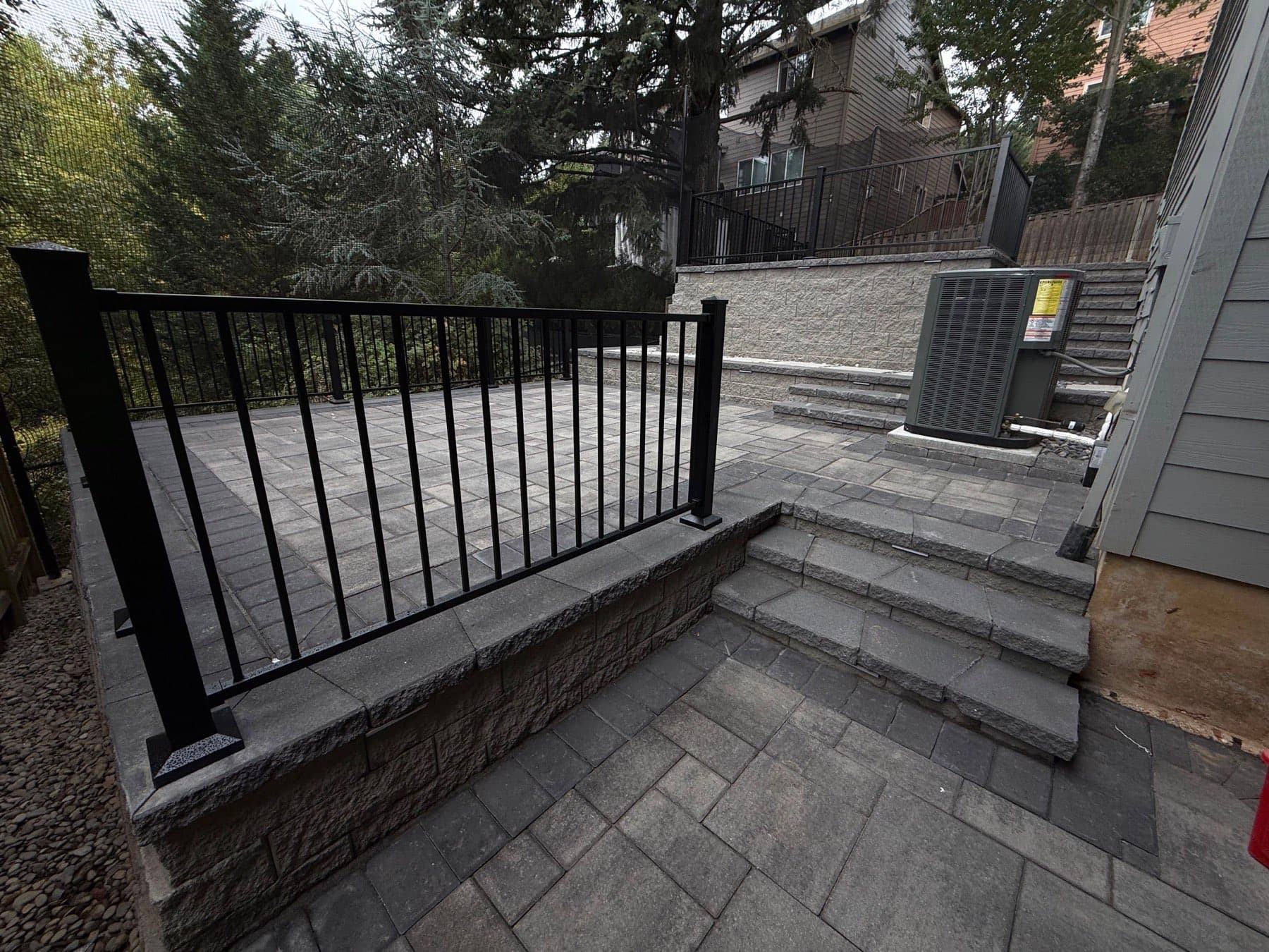 Multi-level paver terraces linked by lit steps and block retaining walls on a steep lot, by GI Landscape