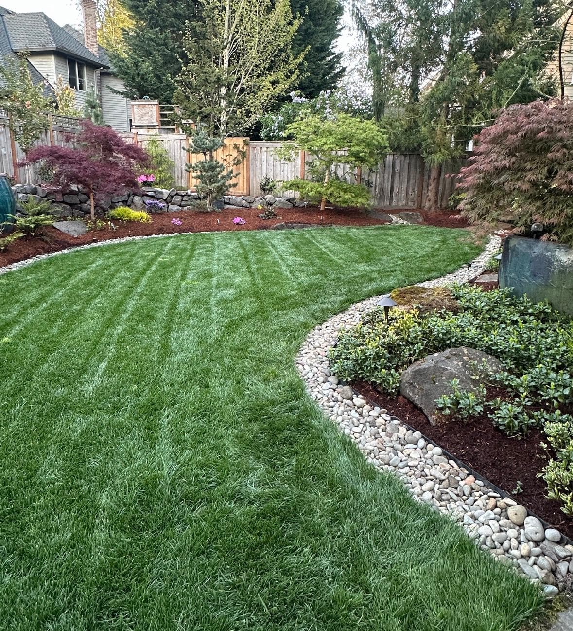 Manicured artificial-turf lawn with a mowing-stripe pattern and a curved planting-bed border, installed by GI Landscape